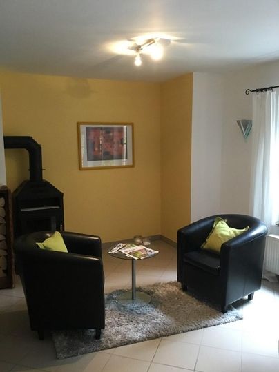 Ein gemütlicher Wohnbereich mit zwei schwarzen Sesseln und einem Glastisch. Die Wände sind gelb gestrichen, und ein Kamin steht in der Ecke.