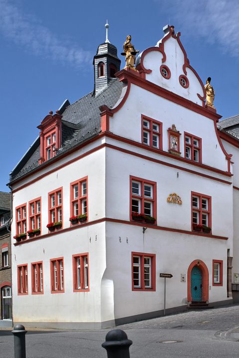 Ein historisches Gebäude mit einer weißen Fassade und roten Akzenten. Es hat viele Fenster und eine auffällige Dachstruktur.
