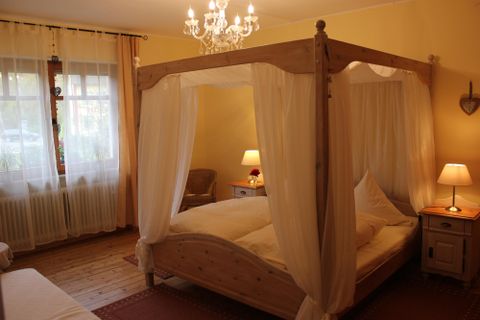 Ein gemütliches Schlafzimmer mit einem Himmelbett und warmen Farben. Weiche Beleuchtung sorgt für eine einladende Atmosphäre.