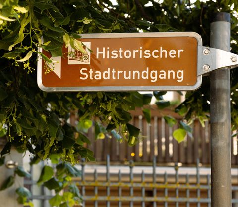 Ein Wegweiser zum historischen Stadtrundgang. Die Schilder ist umgeben von grünen Blättern.
