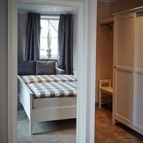 Ein gemütliches Schlafzimmer mit einem Bett und einer Schlafcouch. Der Raum hat große Fenster mit Vorhängen und eine helle, einladende Atmosphäre.