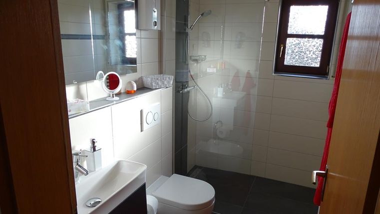 Ein modernes Badezimmer mit Dusche und Waschbecken. Rote Handtücher und ein Teppich verleihen dem Raum einen einladenden Akzent.