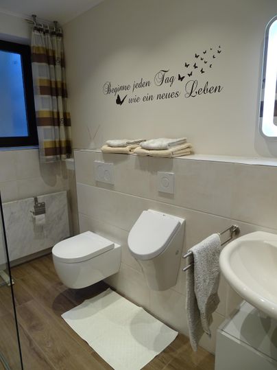 Een moderne badkamer met elegante sanitaire voorzieningen. Aan de muur hangt een motiverende quote en heldere handdoeken zijn netjes geplaatst.