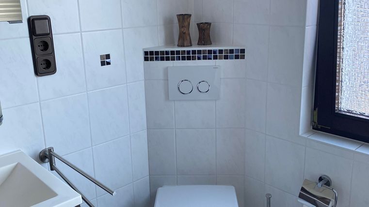 Ein modernes Badezimmer mit weißen Fliesen und einem WC. Neben dem WC befindet sich ein Waschbecken und eine Uhr an der Wand.