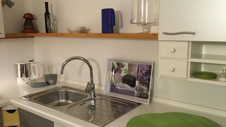 Eine moderne Küche mit einem Edelstahlspülbecken und weißen Schränken. Auf dem Tisch liegen grüne Platzsets und ein dekorierter Bilderrahmen.