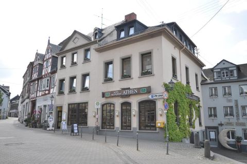 Ein gemütliches Restaurant mit dem Namen "Athen" an einer ruhigen Straßenecke. Umgeben von charmanten Gebäuden und grüner Vegetation.