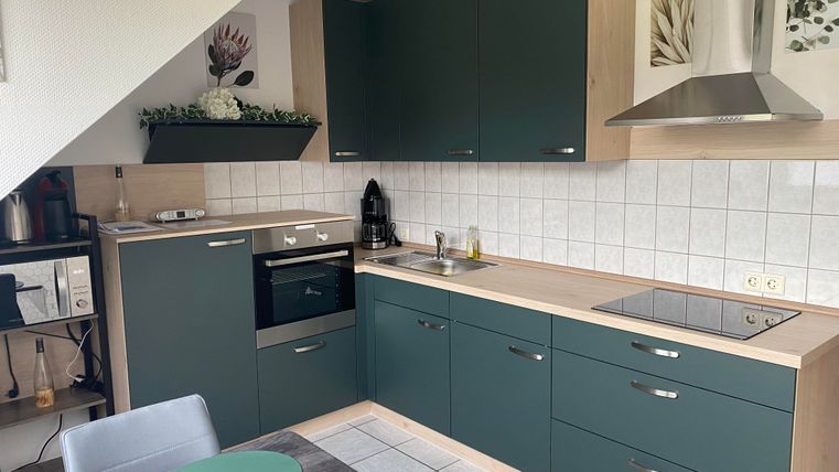 Eine moderne Küche mit grünen Schränken und Edelstahlgeräten. Der Raum ist hell und gut organisiert, mit einem Esstisch im Vordergrund.