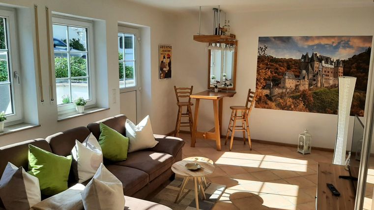Un salon lumineux avec un canapé confortable et des coussins colorés.
Sur le mur, il y a un tableau d'un château, et il y a une petite table avec des chaises.