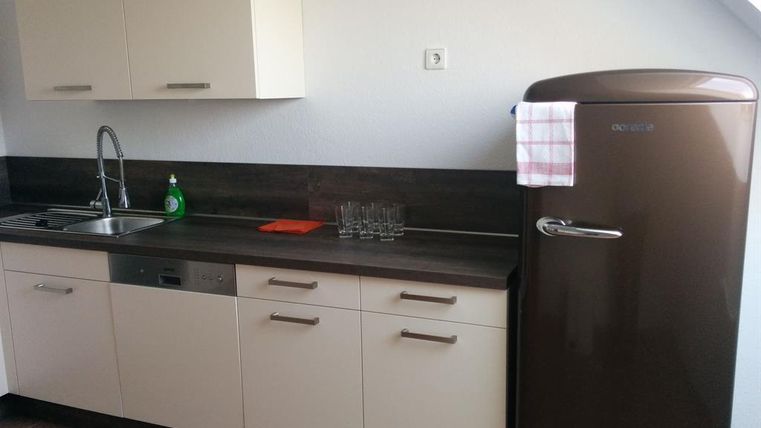 Eine moderne Küche mit weißen Schränken und einem dunklen Arbeitsbereich. Rechts steht ein brauner Kühlschrank mit einem Geschirrtuch.