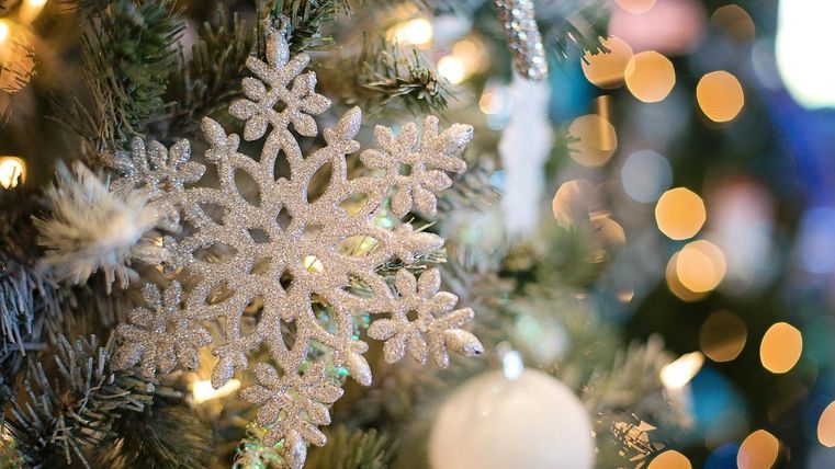 Eine schöne silberne Schneeflockenornament hängt an einem Weihnachtsbaum. Der Hintergrund ist mit bunten Lichtern geschmückt.