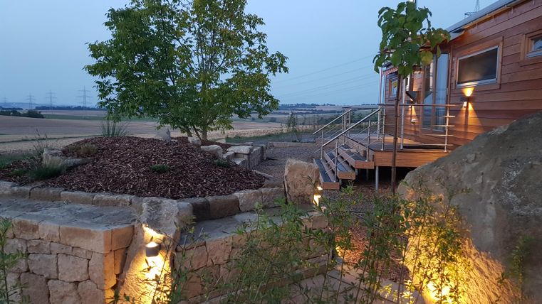 Eine moderne Holzhütte umgeben von einer schönen Landschaft. Ein Baum und sanfte Beleuchtung schaffen eine einladende Atmosphäre.
