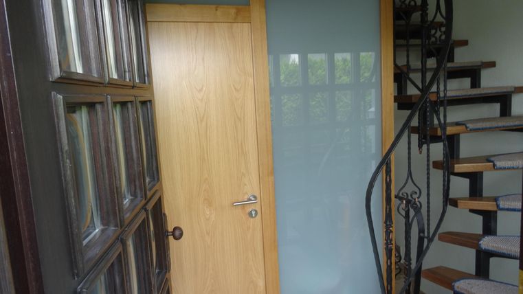 Ein gemütlicher Eingangsbereich mit einer Holztreppe und einer Tür. Die Wände sind in sanften Farben gehalten, und ein Fenster lässt Licht herein.