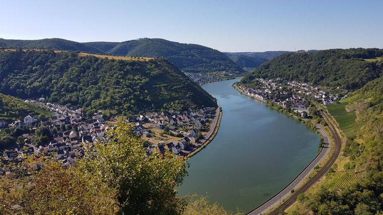 Ein malerischer Fluss, der sich sanft durch grüne Hügel windet. Im Hintergrund ist ein charmantes Dorf am Ufer zu sehen.