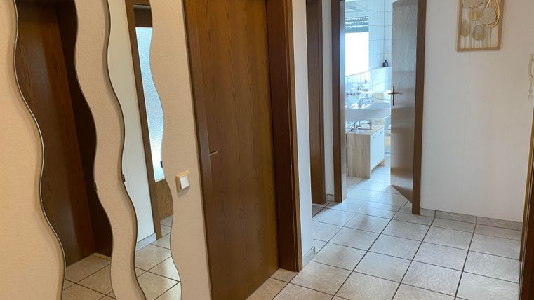 Ein geräumiger Flur mit zwei Türen und einem großen Spiegel. Im Hintergrund ist ein helles Bad zu sehen.