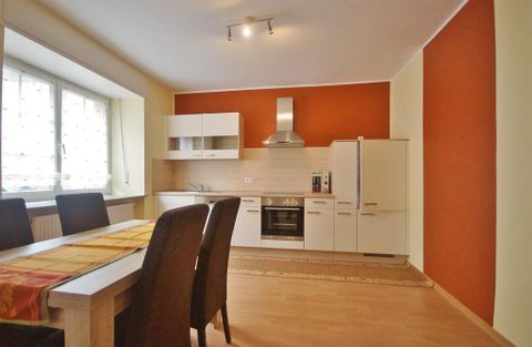 Eine moderne Küche mit weißen Möbeln und einem roten Akzentwand. Der Essbereich ist mit einem Tisch und Stühlen ausgestattet.