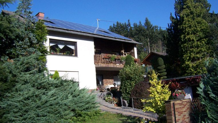 Een mooi huis met een balkon en zonnepanelen. De tuin is groen en goed onderhouden, omringd door bomen.