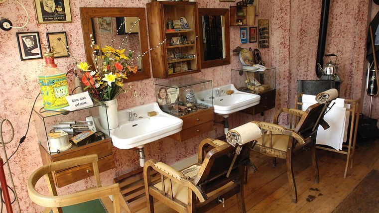 Een kapsalon met twee wasbakken en houten meubels. De muren zijn versierd met afbeeldingen en decoraties.