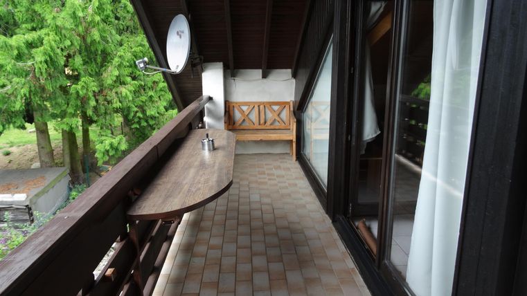 Ein gemütlicher Balkon mit einem langen Tisch und Blick ins Grüne. Die Wände sind aus Holz, und es gibt große Fenster, die Licht hereinlassen.