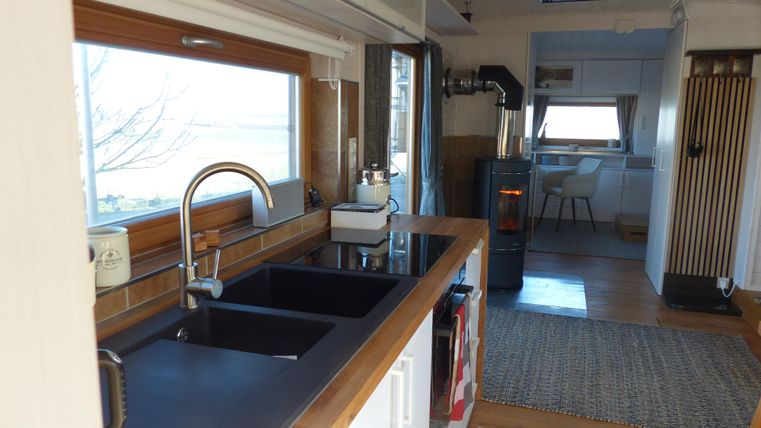 Eine moderne Küche mit einem schwarzen Spülbecken und Holzarbeitsplatte. Im Hintergrund ist ein gemütlicher Wohnbereich mit einem Tisch und einer Heizung sichtbar.