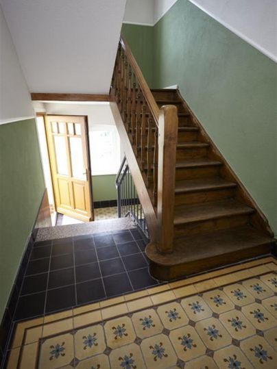 Un escalier avec un escalier en bois et des murs verts. Le sol est décoré d'un revêtement de sol en carrelage coloré et à motifs.