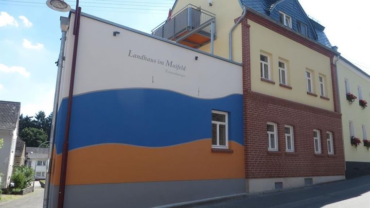 Un bâtiment moderne avec une décoration murale colorée en bleu et orange. Il est situé dans une rue calme avec des fenêtres et un balcon.