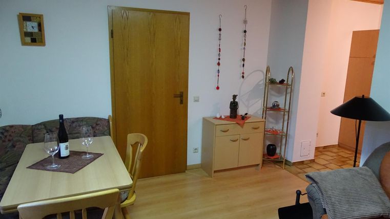 Ein gemütlicher Wohnraum mit einem Esstisch, Stühlen und einer Couch. An der Wand hängt eine Tür, und es gibt eine kleine Dekoration neben einem Regal.