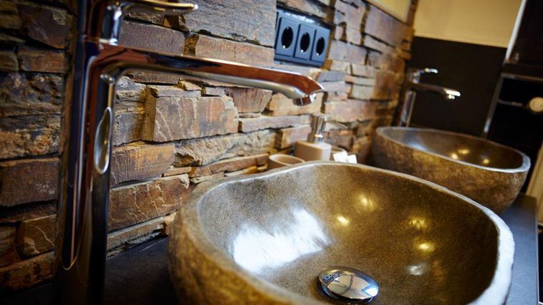 Ein modernes Badezimmer mit zwei runden Waschbecken aus Stein. Die Wände sind mit Naturstein verkleidet und es gibt elegante Wasserhähne.
