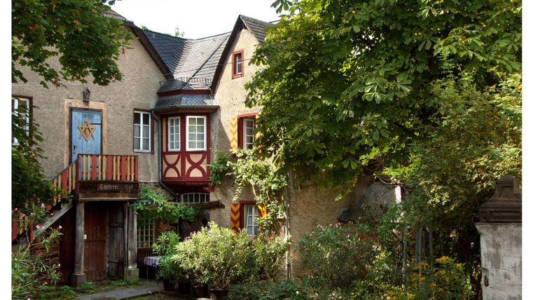 Ein charmantes Haus mit einer bunten Fassade und einem Balkon. Der Garten ist üppig und von Bäumen umgeben.