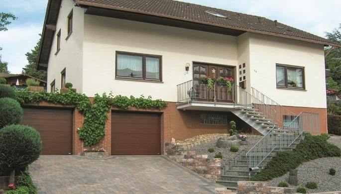 Ein modernes Einfamilienhaus mit zwei Garagen und einer schönen Treppe. Der Garten ist gepflegt und mit grünen Büschen angelegt.