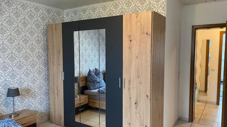 Ein gemütliches Schlafzimmer mit einem großen Kleiderschrank und einem Bett. Die Wände sind mit einem eleganten Muster dekoriert, und es gibt eine sanfte Beleuchtung.