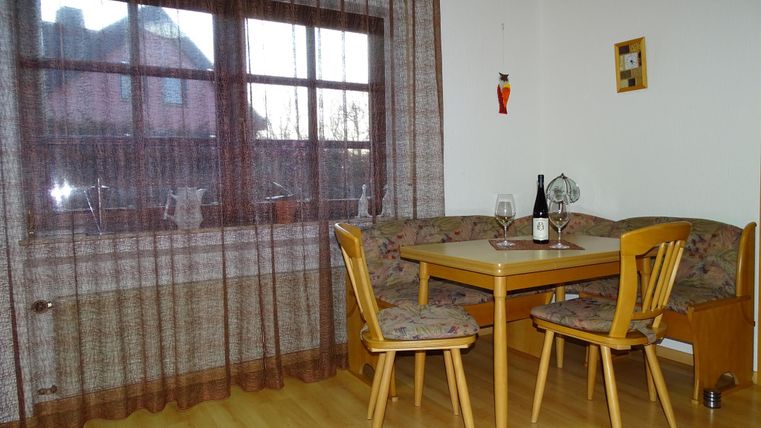 Ein gemütlicher Essbereich mit einem runden Tisch und Stühlen. Am Fenster hängt ein leichter Vorhang und es stehen Wein und Gläser auf dem Tisch.