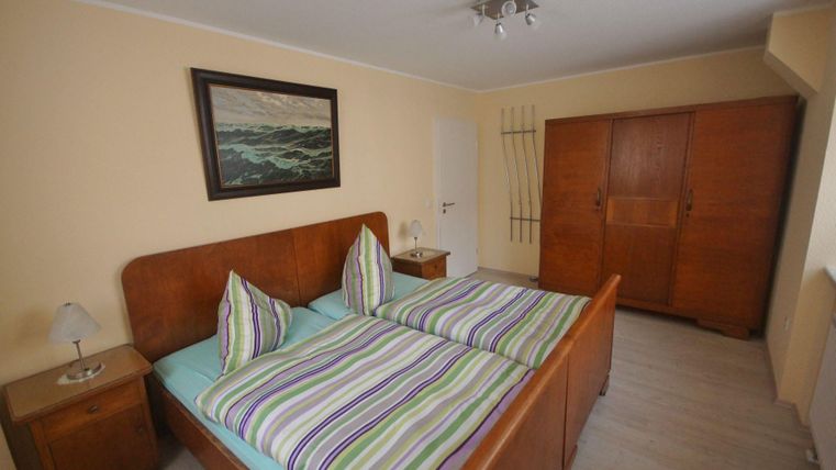 Ein Schlafzimmer mit zwei Betten und gestreiften Bettbezügen. Der Raum ist hell und hat einen Schrank sowie ein Gemälde an der Wand.