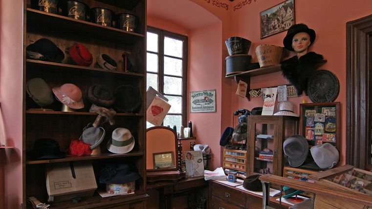 Een traditionele hoedenwinkel met rekken vol hoeden in verschillende stijlen. De muren zijn geschilderd in een warme roze tint en er zijn decoratieve elementen.