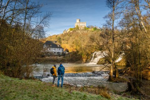 Zwei Personen stehen am Ufer des Elzbachs mit Blick auf die Pyrmonter Mühle und Burg Pyrmont.