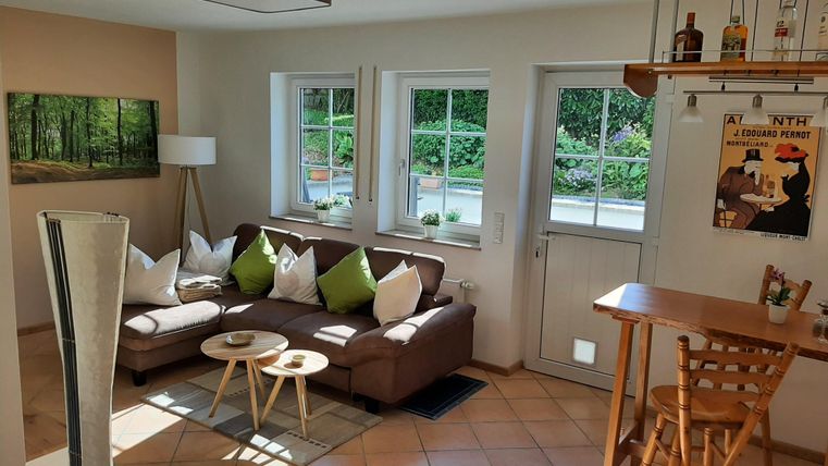 Un salon lumineux avec un canapé confortable et une petite table. De grandes fenêtres laissent entrer beaucoup de lumière et offrent une vue sur le jardin.