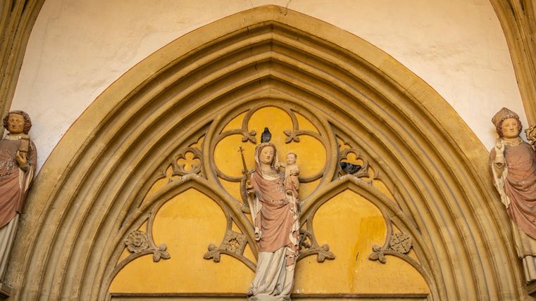 Eine historische Kirchenfassade mit kunstvollen Steinmetzarbeiten und Figuren an den Seiten. In der Mitte steht eine Statue, die eine wichtige religiöse Figur darstellt.