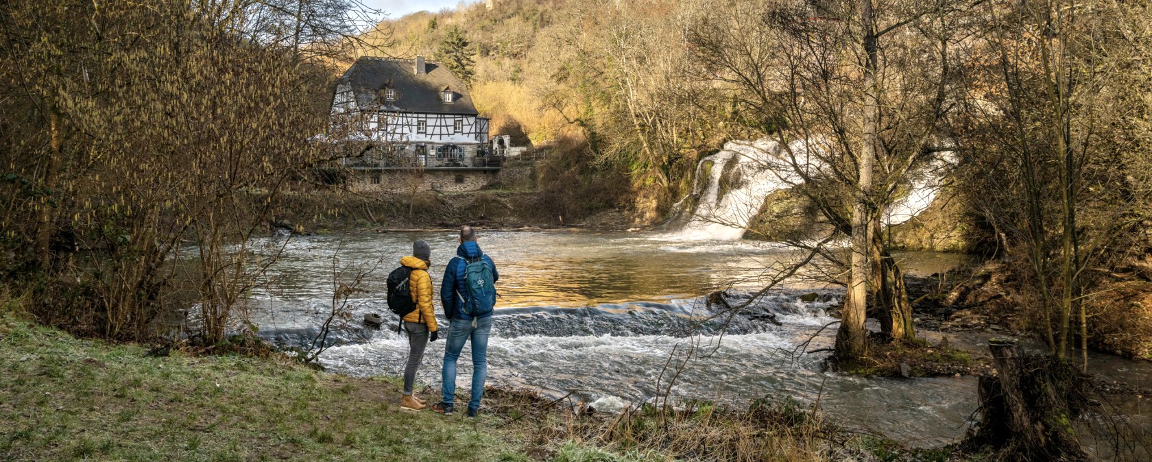 Zwei Personen am Elzbach, mit Blick auf die Pyrmonter M&uuml;hle und Burg Pyrmont. Herbstliche Landschaft mit Wasserfall und Fachwerkhaus., &copy; Eifel Tourismus GmbH, D. Ketz