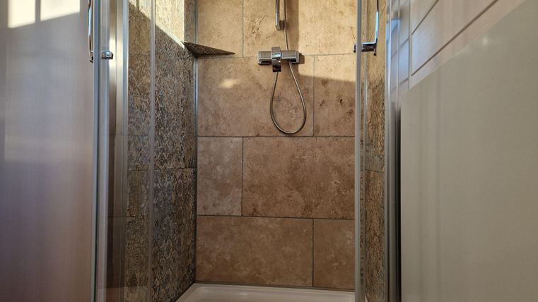 Eine moderne Duschkabine mit Fliesen und einem klaren Duschkopf. Das Licht fällt sanft auf die Wände und schafft eine einladende Atmosphäre.