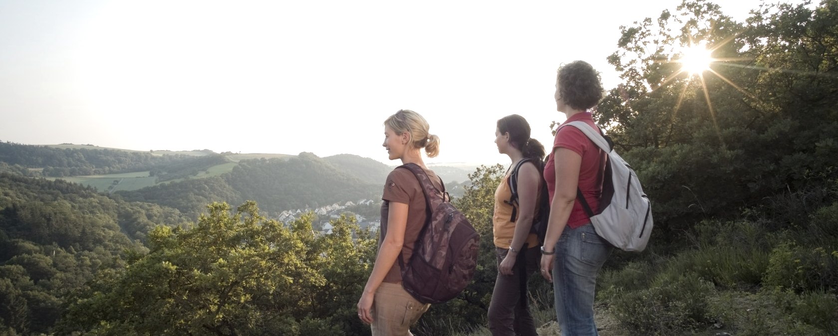 Drei Frauen mit Rucksäcken genießen den Ausblick von einem Hügel in der Trimbser Schweiz bei Sonnenuntergang., © Traumpfade