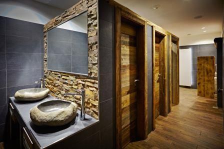 Ein modernes Badezimmer mit steinernen Waschbecken und Holzverkleidungen. Die Wände sind in dunklen Farben gehalten, was eine elegante Atmosphäre schafft.
