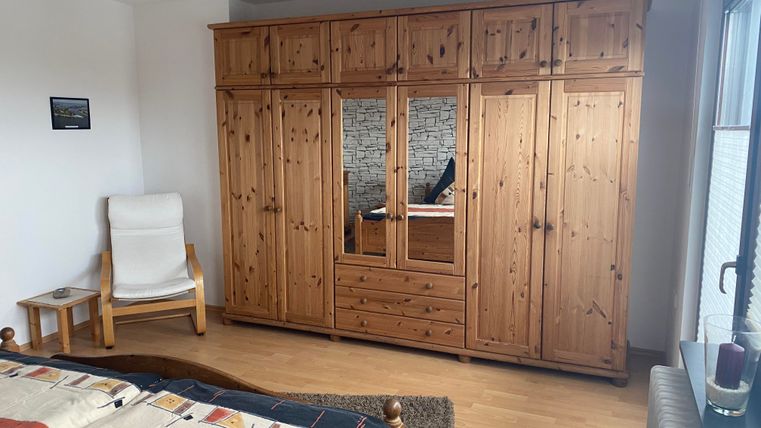 Ein gemütliches Schlafzimmer mit einem großen Holzschrank und einem bequemen Stuhl. Der Boden ist aus Holz und das Zimmer wirkt freundlich und einladend.