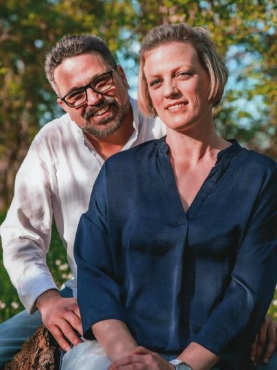 Ein Paar sitzt entspannt im Freien. Sie lächeln und genießen die Natur im Hintergrund.