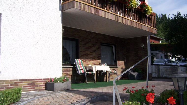 Een gezellige balkons met bloemen en twee stoelen. De entree is ingericht met stenen en kleurrijke bloemen.