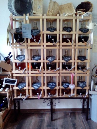 Eine Holzregalwand mit mehreren Flaschen und Tafeln. Die Flaschen sind kreativ beschriftet und in einem rustikalen Geschäft ausgestellt.