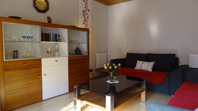 Een lichte woonkamer met een gezellige zithoek en een zwarte salontafel. De muren zijn eenvoudig, en er is een houten plafond en decoratieve elementen.