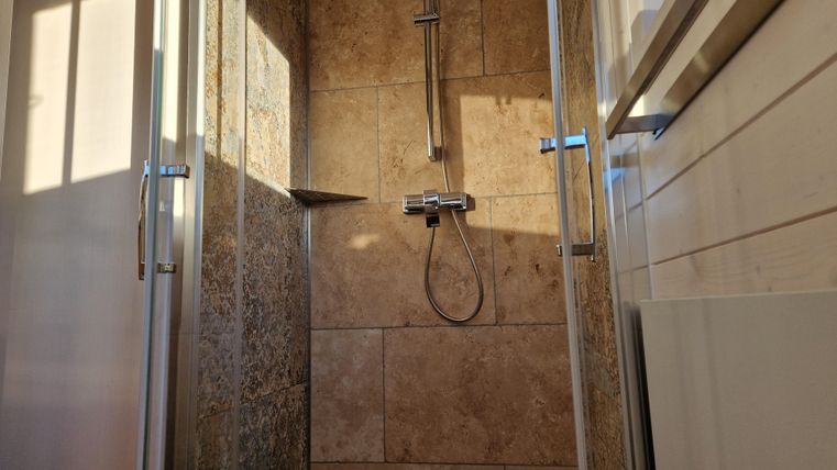 Eine moderne Duschkabine mit hellen Fliesen und einem Handbrauseset. Das Licht strömt durch das Glas, was eine einladende Atmosphäre schafft.