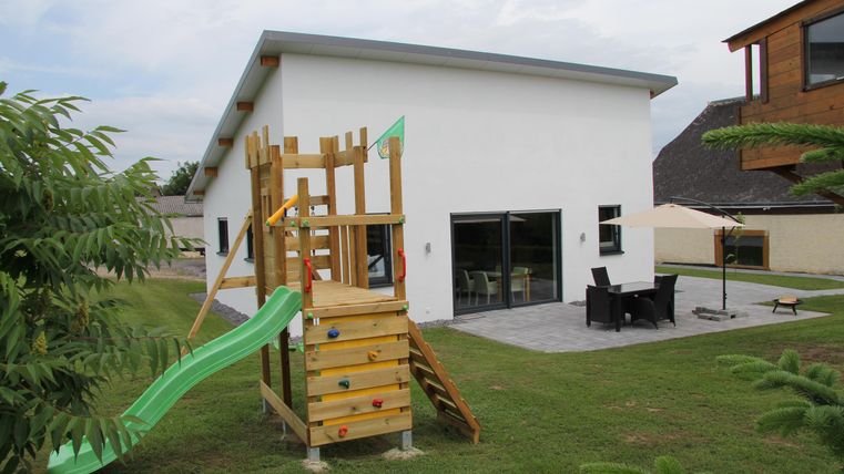 Une maison moderne avec une structure de aire de jeux dans le jardin. Le toboggan du aire de jeux est vert et l'environnement est vert et accueillant.
