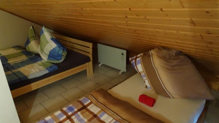 Ein gemütliches Dachzimmer mit zwei Betten und einem Holzdach. Die Bettwäsche ist kariert und es gibt Kissen und Decken.