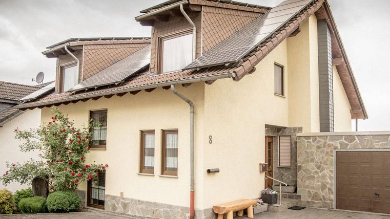 Ein modernes Einfamilienhaus mit einer hellen Fassade und einem Pultdach. Vor dem Haus befinden sich Grünpflanzen und ein gepflasterter Weg.