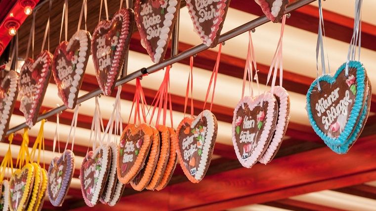 Eine bunte Auswahl an Lebkuchenherzen hängt an einem Marktstand. Jedes Herz hat eine liebevolle Botschaft und ist mit buntem Zuckerguss verziert.